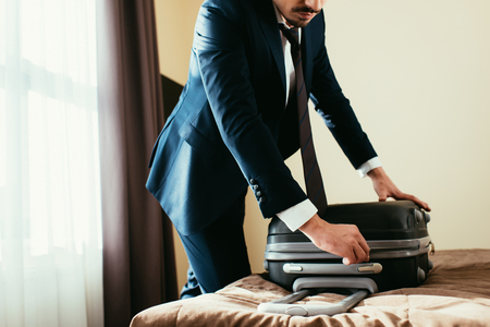 cropped view of businessman in suit with suitcase on bed in hotel roomの写真素材