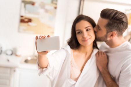 beautiful couple kissing and taking selfie on smartphone at homeの写真素材