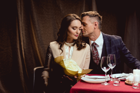 beautiful couple sitting at table with flower bouquet during romantic date in restaurantの写真素材