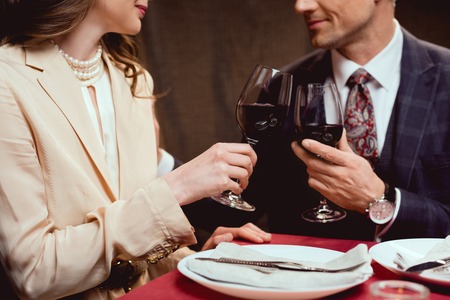 partial view of couple clinking glasses of red wine during romantic date in restaurantの写真素材