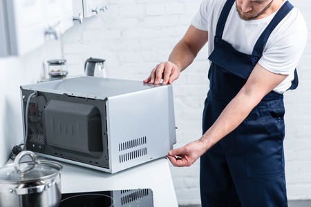 partial view of adult handyman repairing microwave oven in kitchenの写真素材