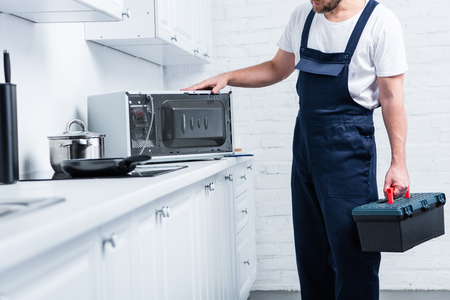 cropped shot of handyman with toolbox checking microwave oven in kitchenの写真素材