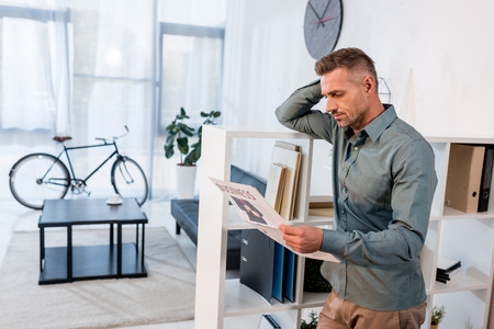 handsome businessman standing and reading business newspaper in modern office