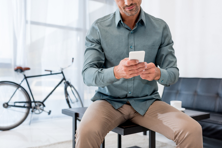 cropped view of businessman sitting on coffee table and using smartphoneの写真素材