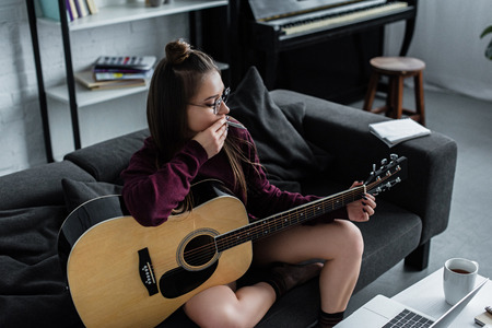 girl sitting on couch with guitar and smoking marijuana joint in living roomの写真素材