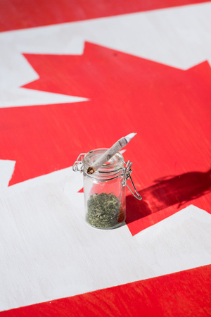 selective focus of cannabis in glass jar with joint on canadian flag, marijuana legalization conceptの写真素材