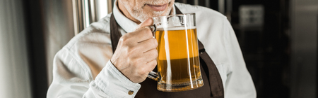 cropped view of senior brewer testing beer in brewery