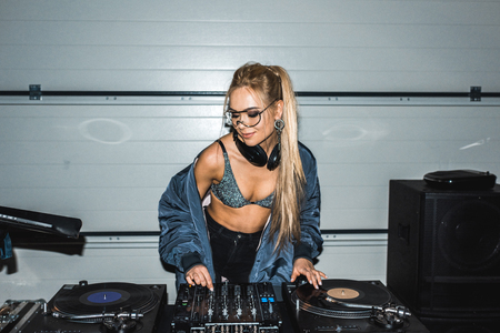 attractive dj woman in glasses standing and looking at vinyl recordsの写真素材