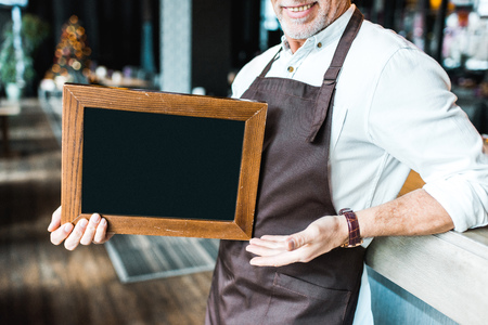 cropped view of senior owner of pub holding empty board and standing near bar counterの写真素材