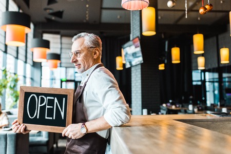 owner of pub holding open sign and standing near bar counterの写真素材