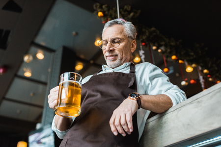male worker in apron holding glass of beer in pubの写真素材