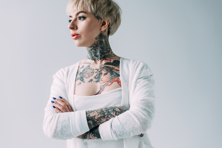 attractive woman with tattoos standing with crossed arms isolated on greyの写真素材