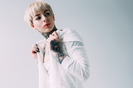 confident woman with tattoos standing isolated on grey