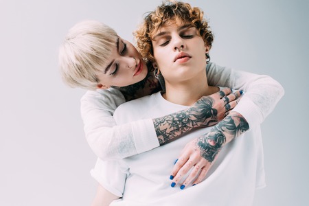 attractive girl hugging boyfriend with curly hair isolated on grey