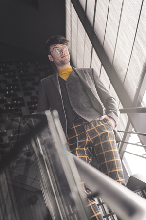 cheerful stylish man in glasses standing with hand in pocket on stairsの写真素材