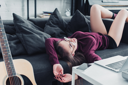 attractive girl in glasses lying on sofa in living roomの写真素材