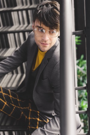 dreamy young man in glasses sitting on stairsの写真素材