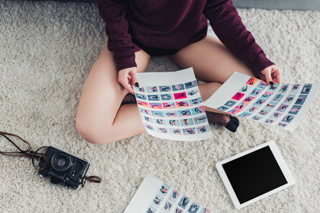 cropped view of photographer sitting on carpet and holding picturesの写真素材