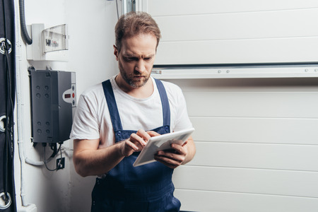serious adult electrician using digital tablet near electrical boxの写真素材