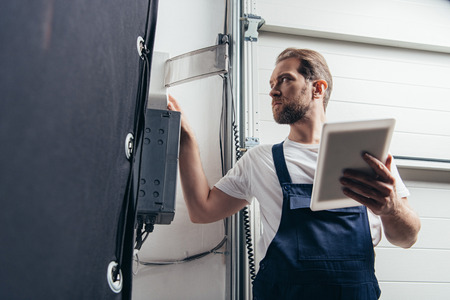 low angle view of male bearded repairman with digital tablet checking electric boxの写真素材