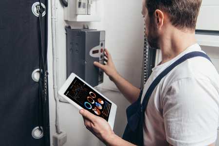 male electrician holding digital tablet with graphs on screen and checking electric boxの写真素材