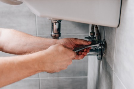 cropped shot of male plumber in working overall fixing sink by spanner in bathroomの写真素材