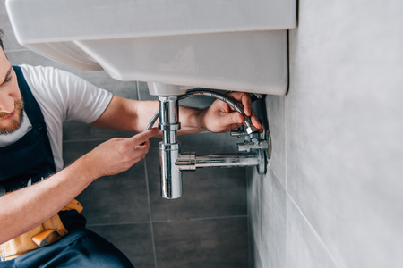 partial view of male plumber in working overall fixing sink in bathroomの写真素材
