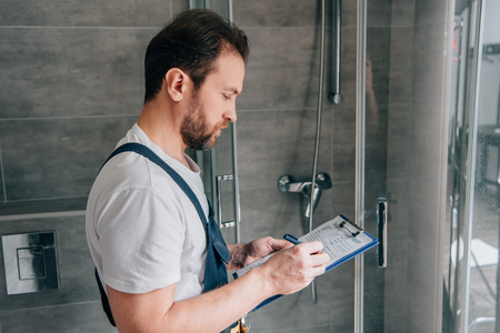 side view of male plumber making notes in clipboard while checking shower in bathroomの写真素材