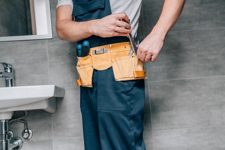 cropped shot of male plumber putting wrench in toolbelt in bathroomの写真素材