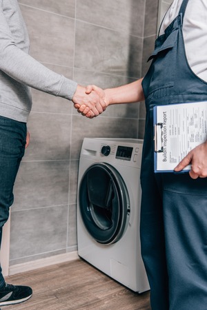 cropped shot of male handyman with clipboard shaking hands with owner in bathroom