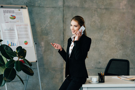 smiling businesswoman talking on smartphone while standing by work desk deskの写真素材