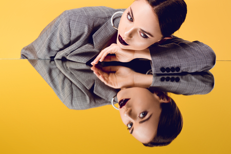 beautiful glamorous woman in formal wear looking at mirror reflection isolated on yellowの写真素材