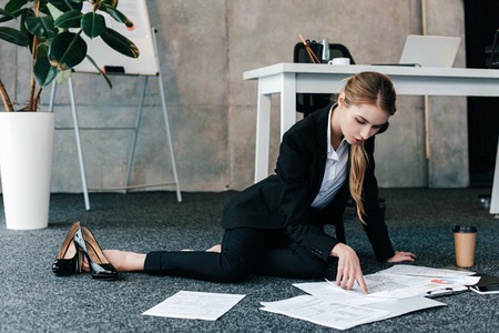 barefoot businesswoman sitting on floor near work-table and reading documentsの写真素材