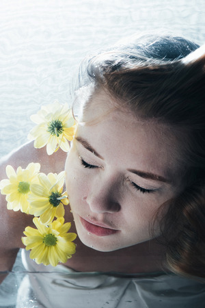 close up of beautiful woman posing underwater with yellow flowersの写真素材