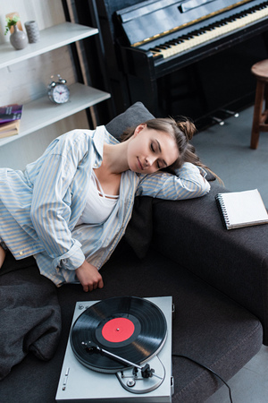 attractive girl sleeping on sofa near vintage record player at homeの写真素材