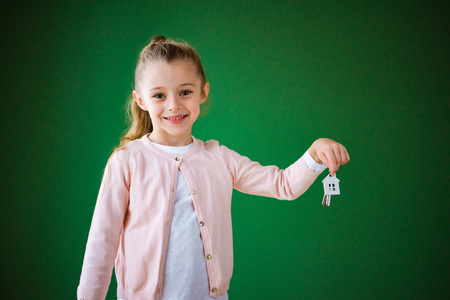 smiling kid holding house shaped key chain on green backgroundの写真素材