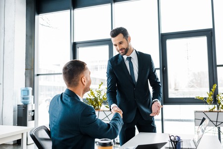 handsome businessman shaking hands with coworker in modern office