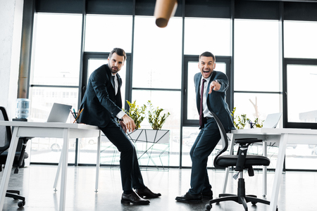 cheerful businessman in formal wear pointing with finger at falling paper cup  in modern officeの写真素材