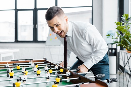 excited businessman in formal wear screaming while  playing table footballの写真素材