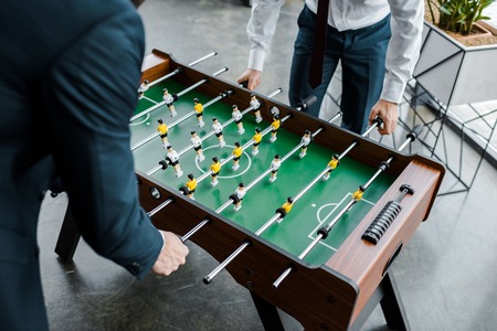cropped view of businessmen in formal wear playing table football