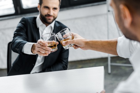 selective focus of businessman toasting glasses of whiskey with coworkerの写真素材