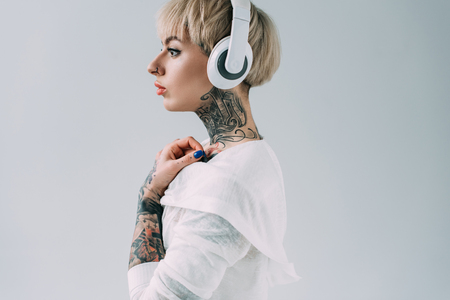 side view of attractive woman listening music in headphones isolated on greyの写真素材