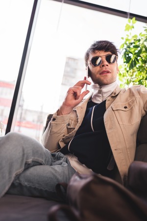 trendy man in sunglasses talking on smartphone in cafeの写真素材
