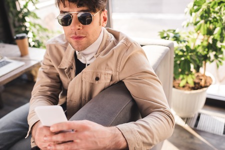 selective focus of trendy man in sunglasses using smartphone in cafeの写真素材