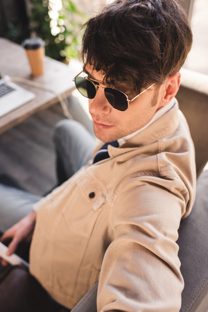 selective focus of trendy man in sunglasses sitting in cafeの写真素材