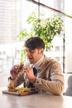 cheerful man eating tasty burger in cafeの写真素材