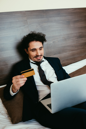 smiling businessman shopping online with credit card and laptop in hotel roomの写真素材