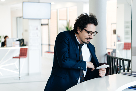 businessman with smartphone standing at reception desk for check-in at the hotelの写真素材
