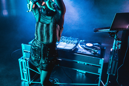 dj woman covering face while standing near dj equipment in nightclub with smoke