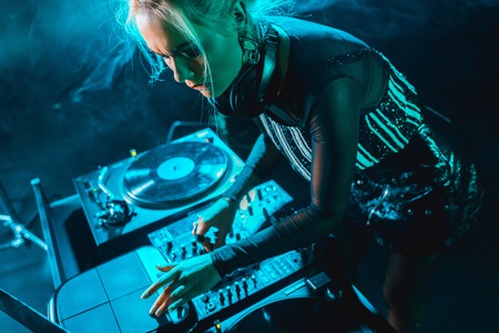 focused beautiful dj girl using dj equipment in nightclub with smokeの写真素材